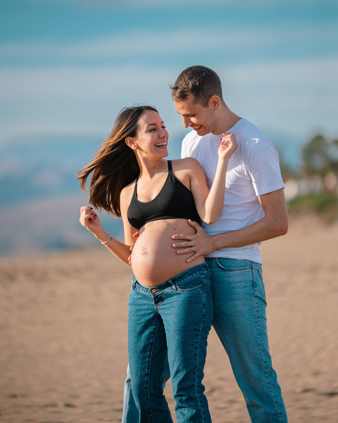 Photo Shoot A pregnant man and woman standing on the beach.