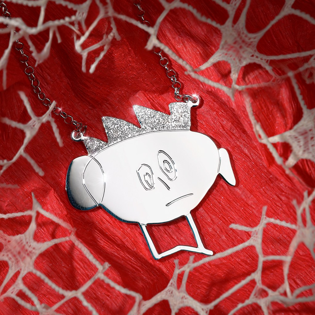 Privezak u obliku pileta na crvenoj pozadini.