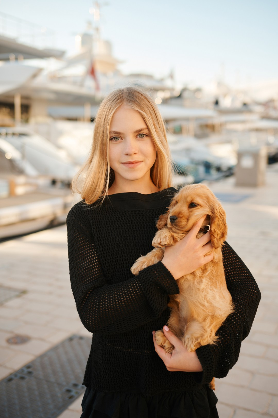 Happy little girl holding puppy on sunny day by yachts in Cannes