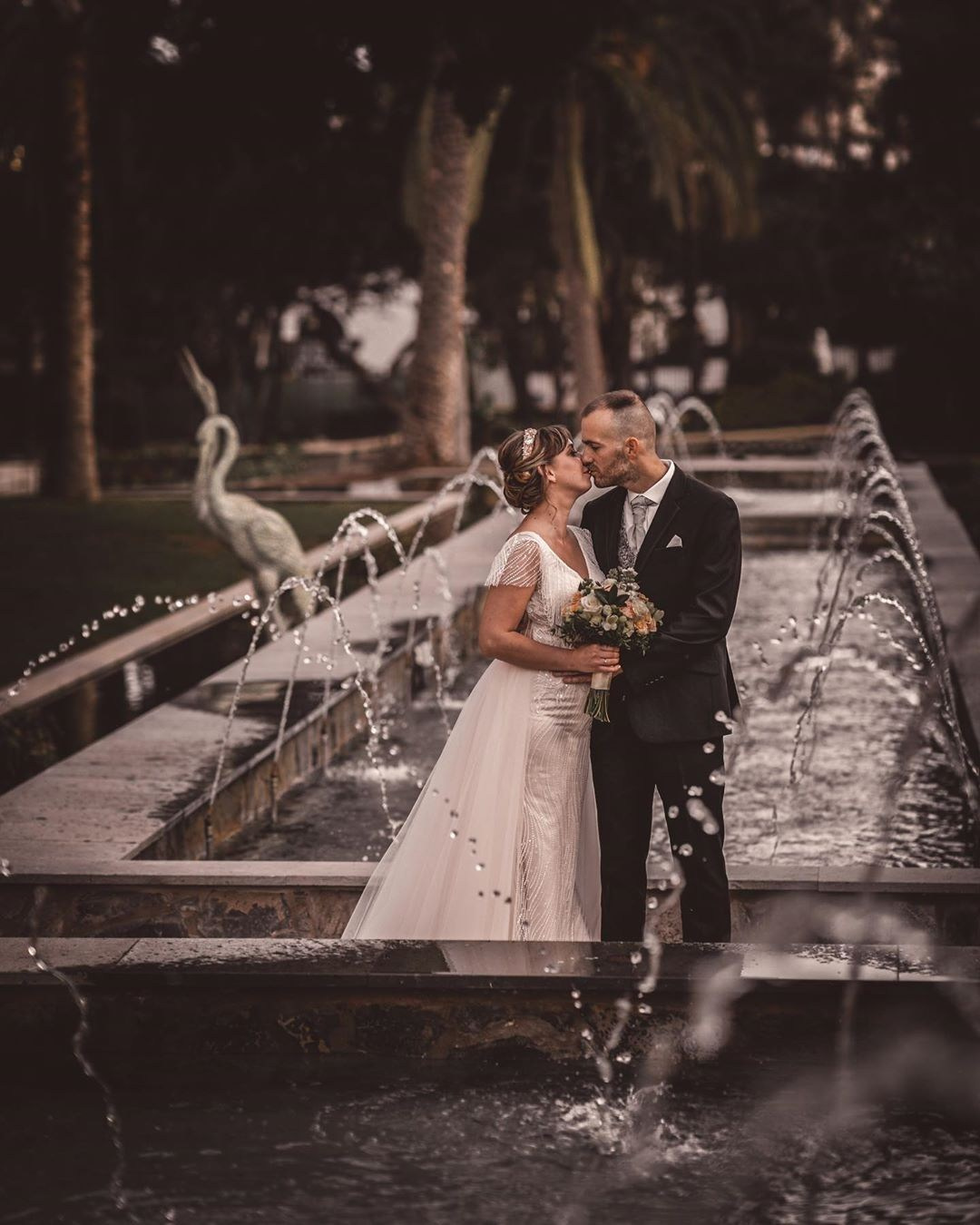 A bride and groom kissing in front of a fountain.