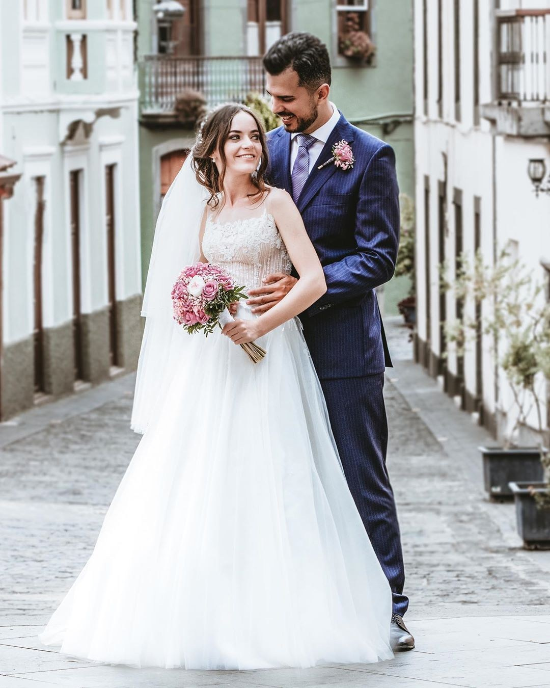 A bride and groom are embracing on a cobblestone street.