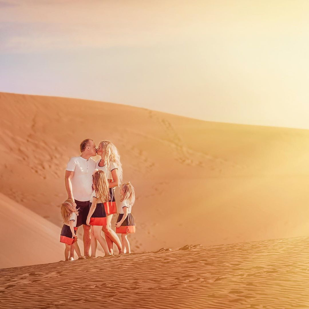 Une famille se tient au sommet d'une dune de sable au coucher du soleil.