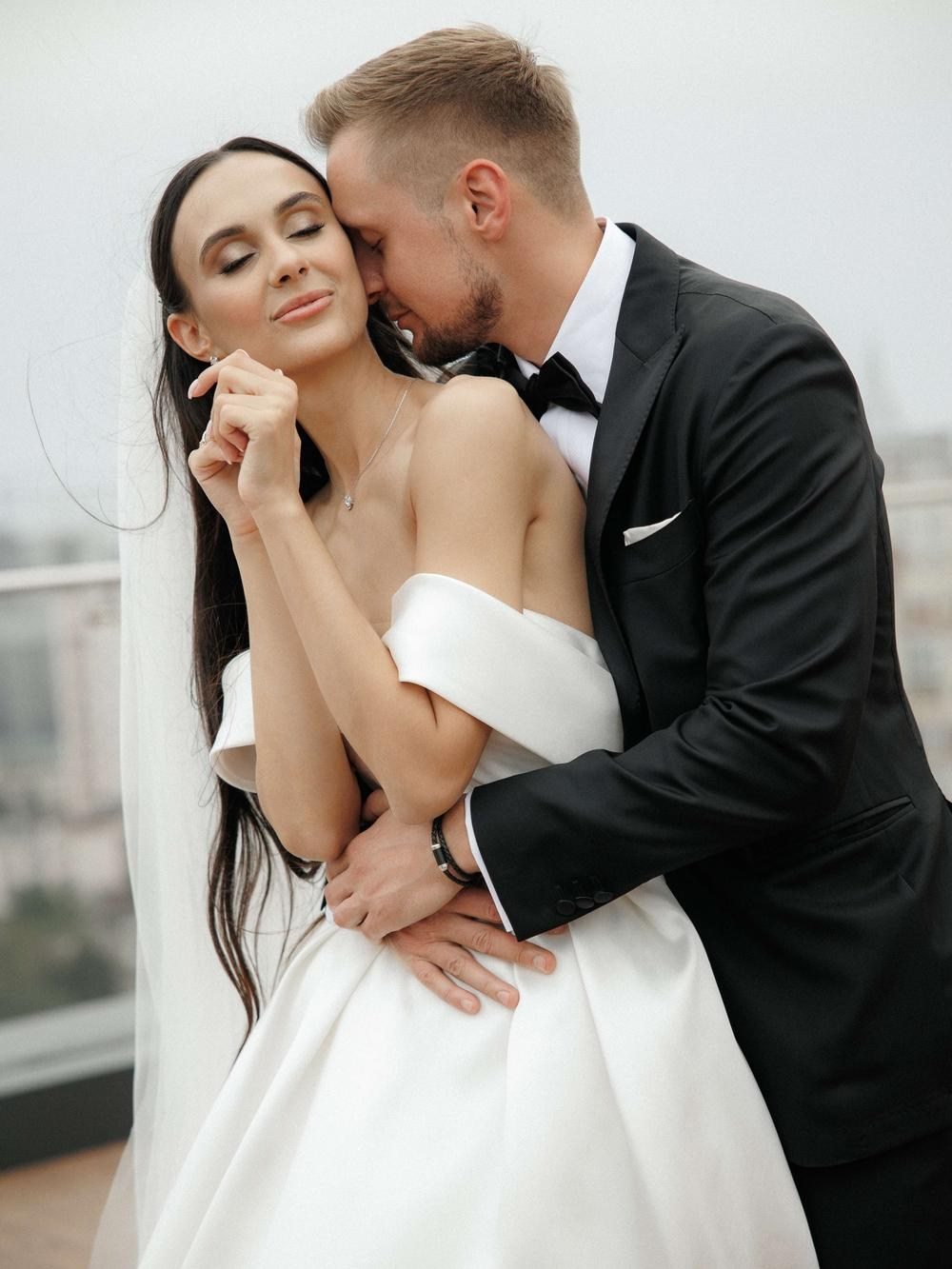 Stylish groom in tuxedo kisses bride in Tuscany