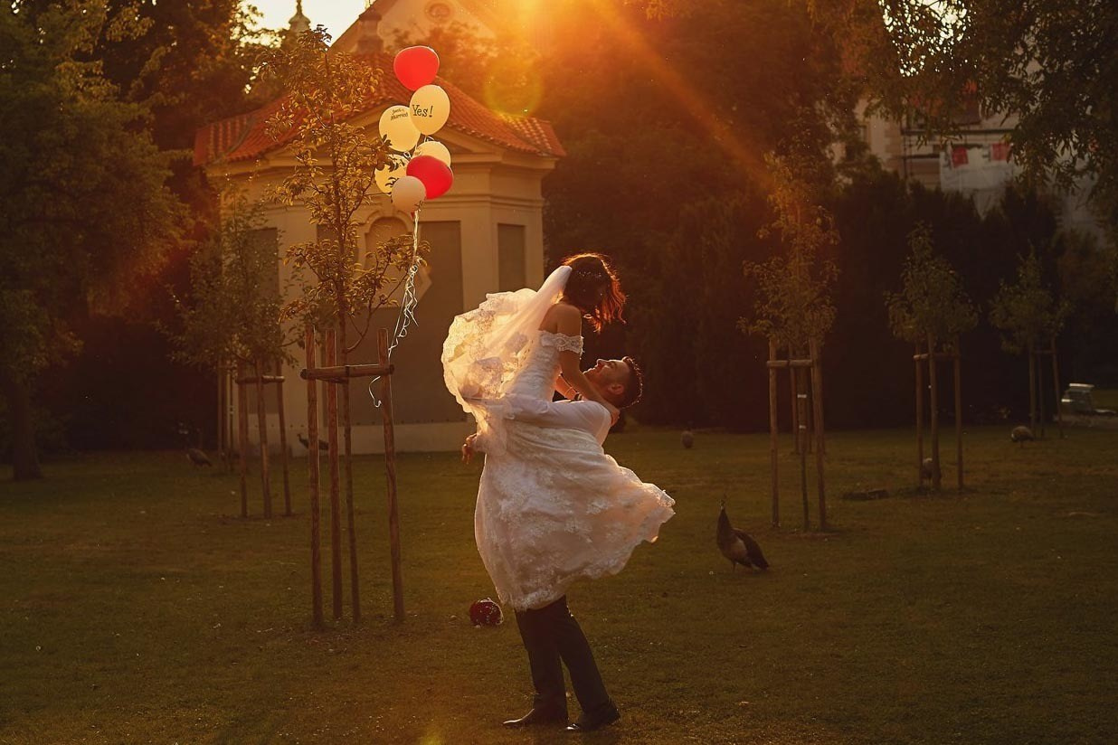 Israeli groom spinning bride under golden light, peacocks observing in a secret garden in Prague.