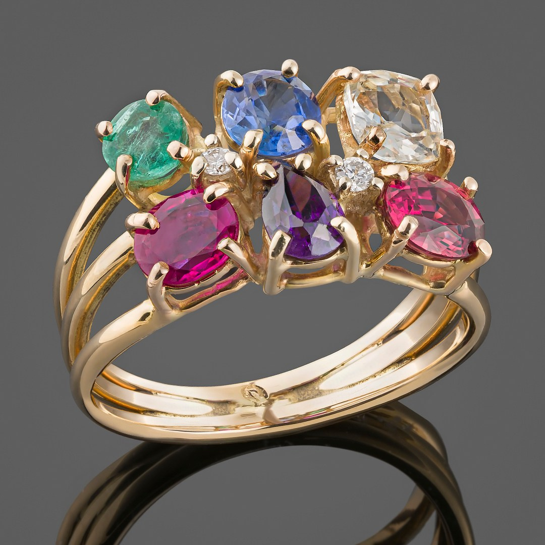 Zlatni prsten sa dragim kamenjem na sivoj pozadini.