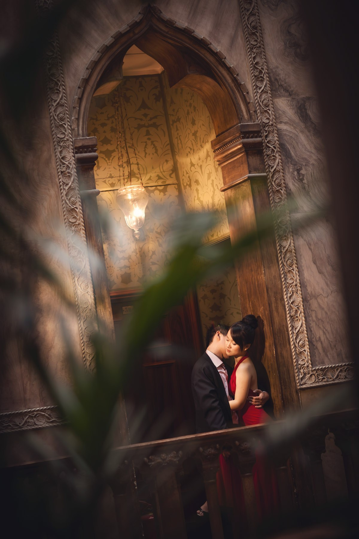 A man embraces his red dress wearing Thai fiancee for a sexy kiss in the historic Hotel Danieli in the heart of Venice during their Love Story Adventures.