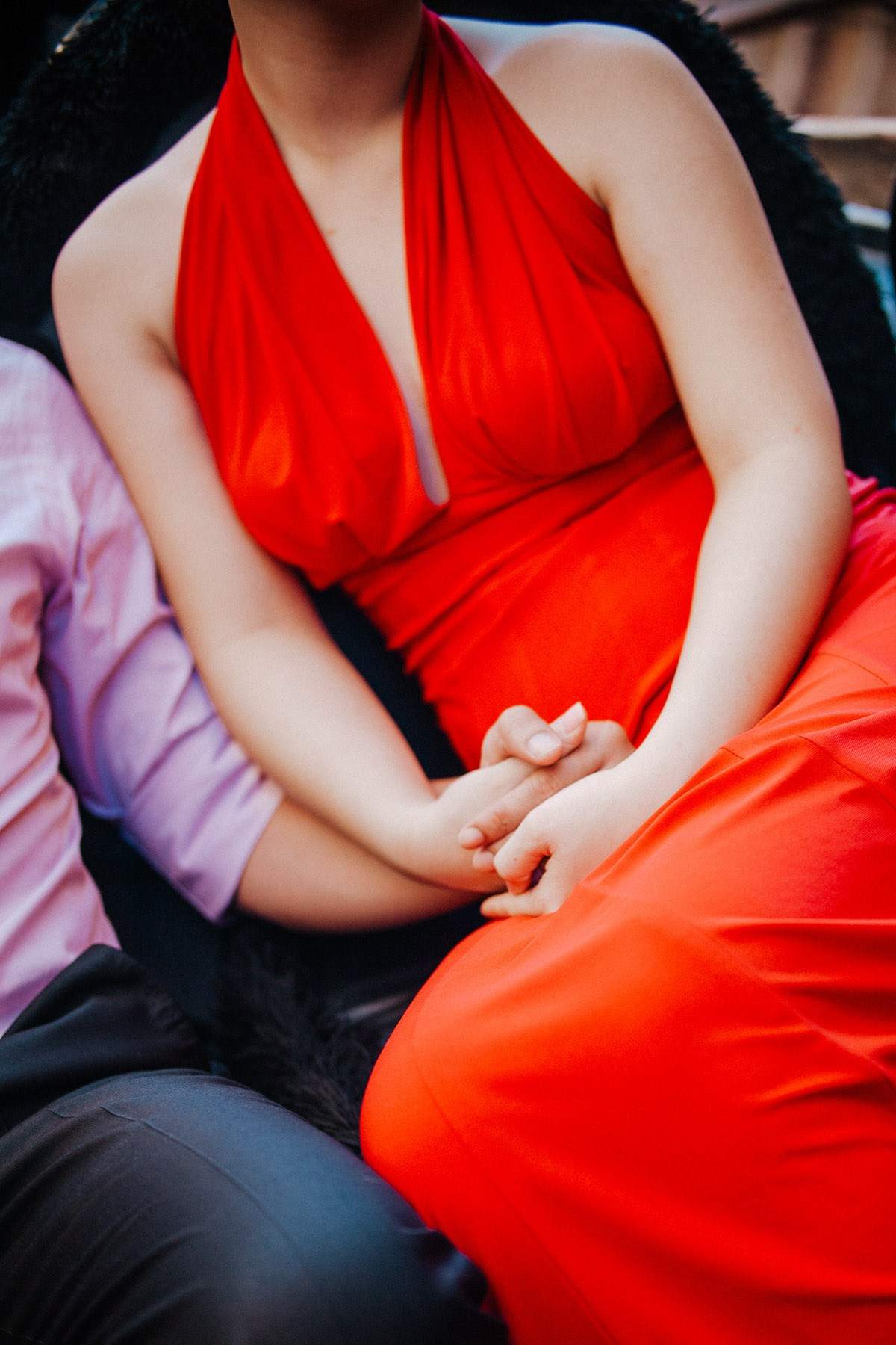 A Thai woman wearing a bold red dress holds hands with her fiancee as they explore the canals of Venice in a gondola.