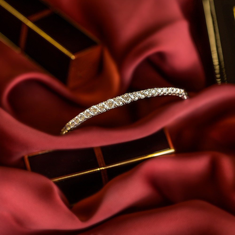 Zlatna narukvica sa dijamantima uspravljena na svili pored karmina.