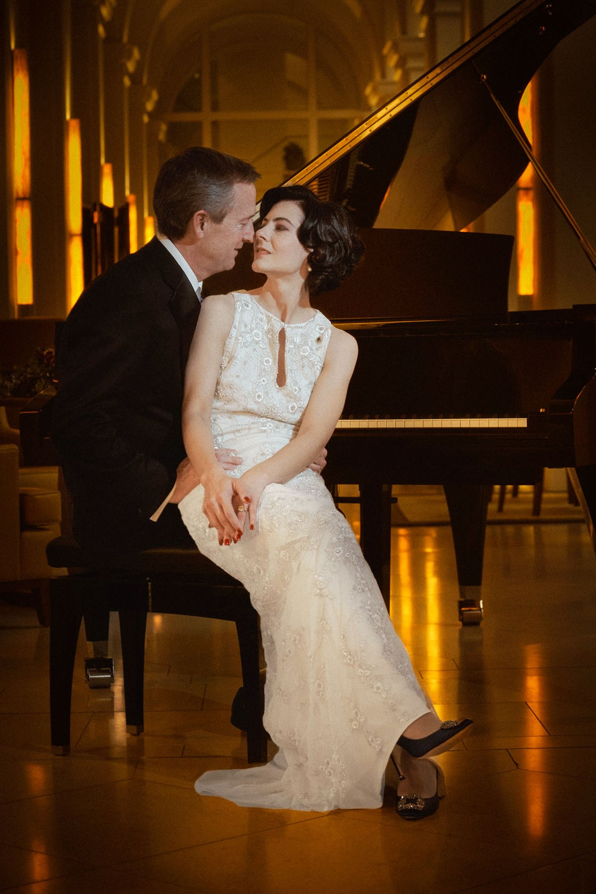 Chicago bride sitting on husband's lap by black baby grand piano at Mandarin Oriental, Prague.