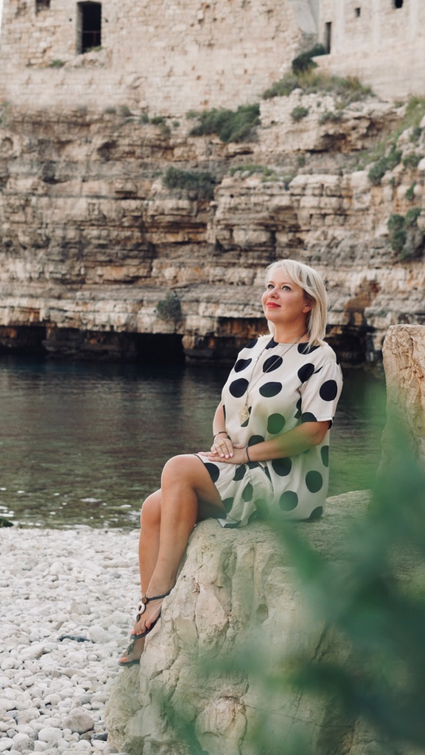 Donna in piedi sulla spiaggia a Polignano a Mare, godendosi la vista sul mare.