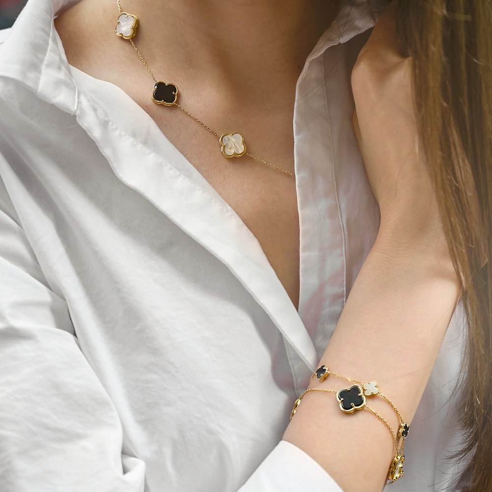 Zlatna narukvica i ogrlica na devojci u beloj košulji.