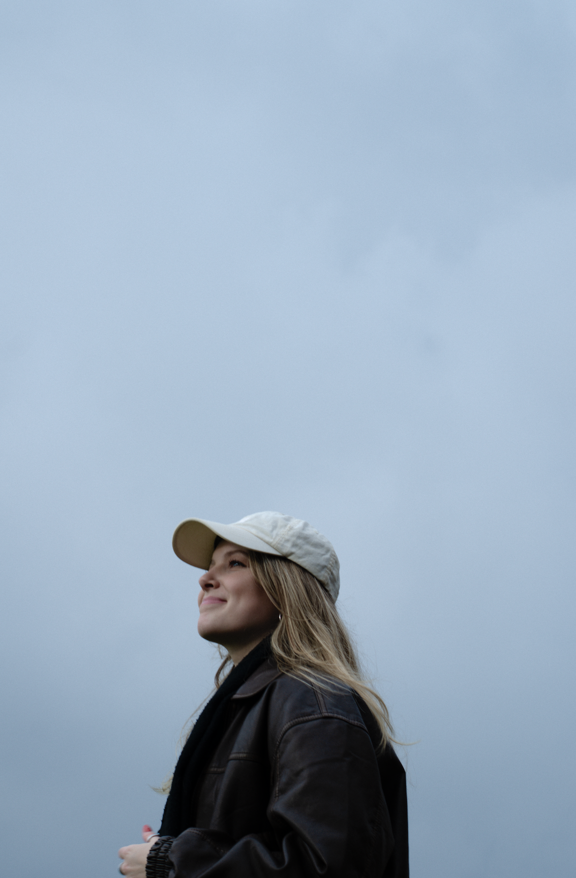 Porträt einer jungen Frau mit blonden Haaren und Kappe vor einem blau-grauen Hintergrund