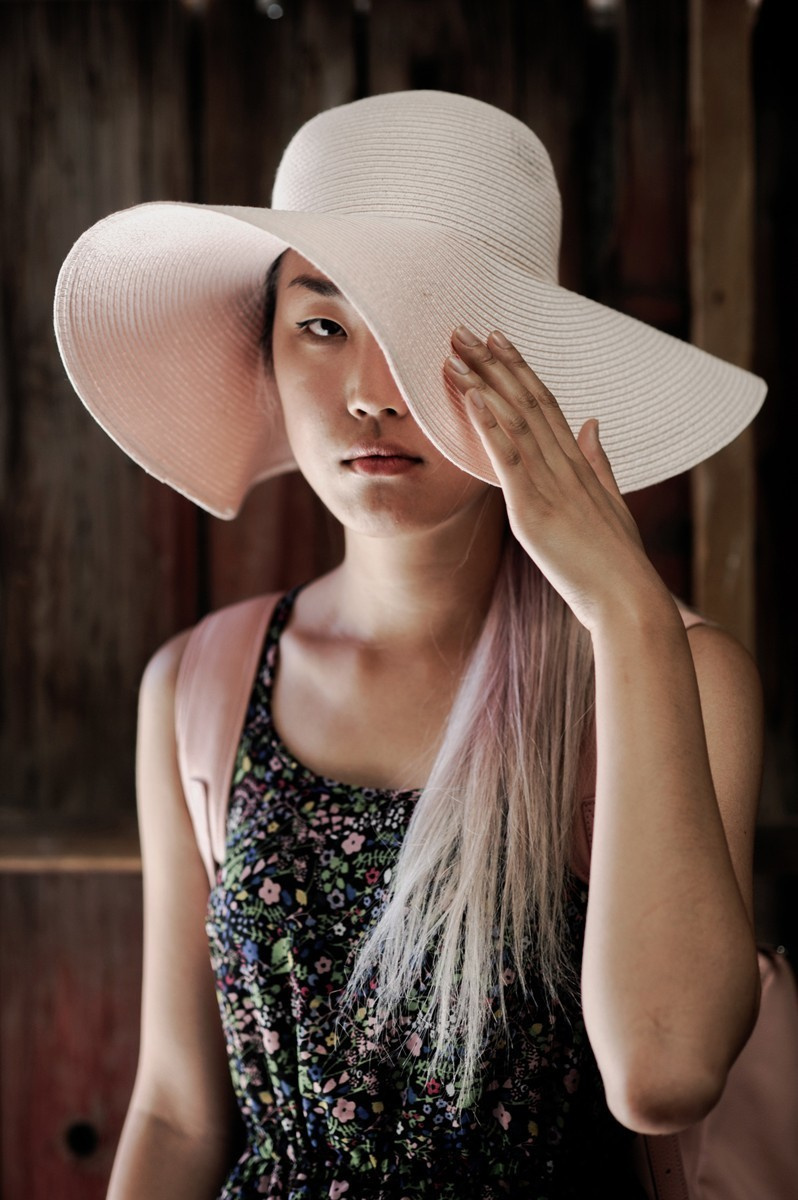 Portrait of a young woman in a large white hat and floral dress.