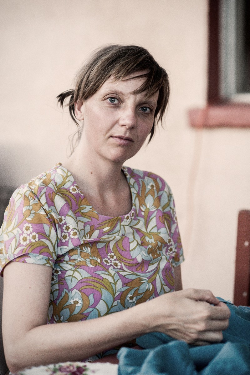 Portrait of a young woman busy sewing, against the wall of an old house.