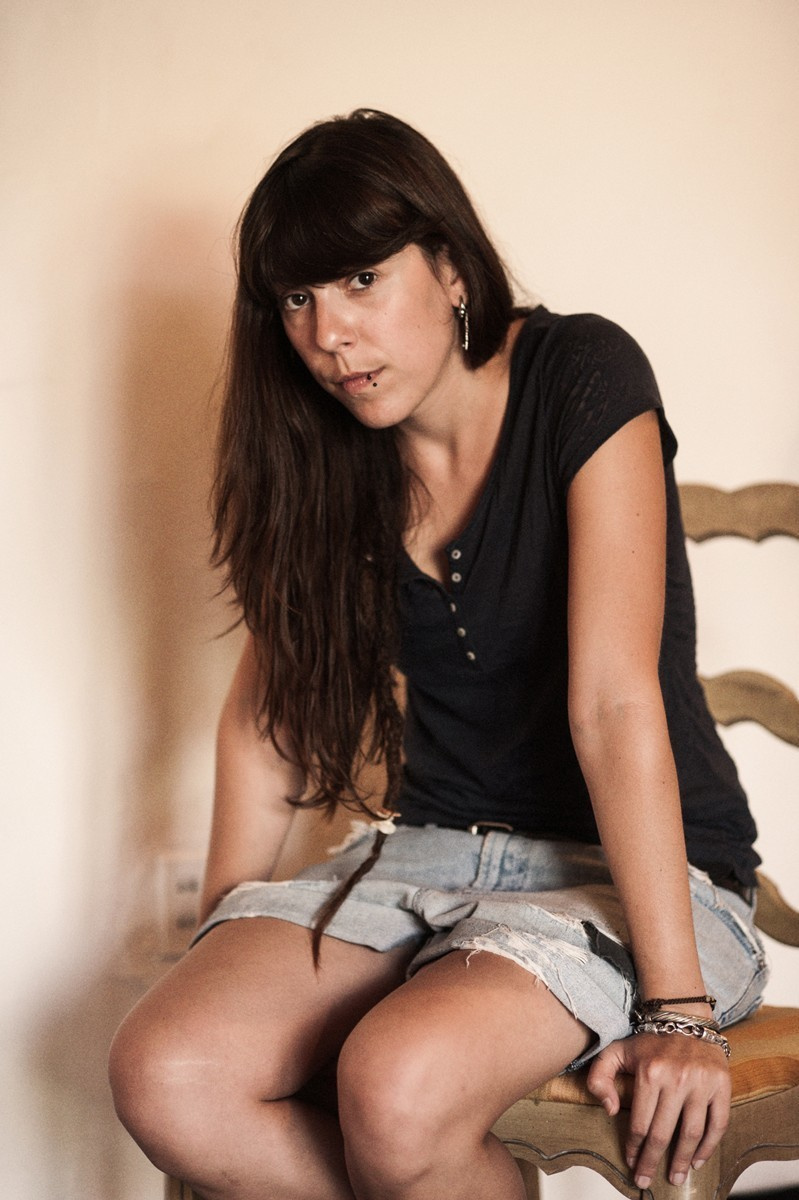 Girl with long black hair poses for a photographer sitting on a chair.