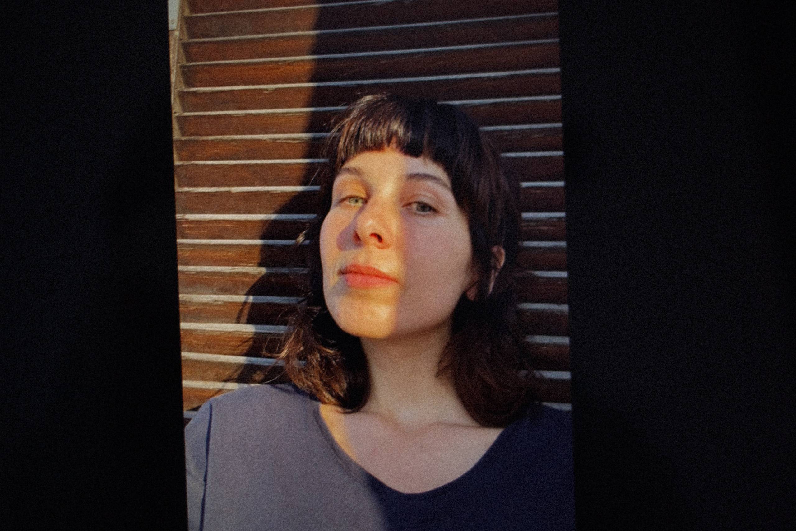 Un retrato dramático de una mujer apoyada en una puerta de madera, con una luz intensa y contrastada que resalta su rostro y rasgos