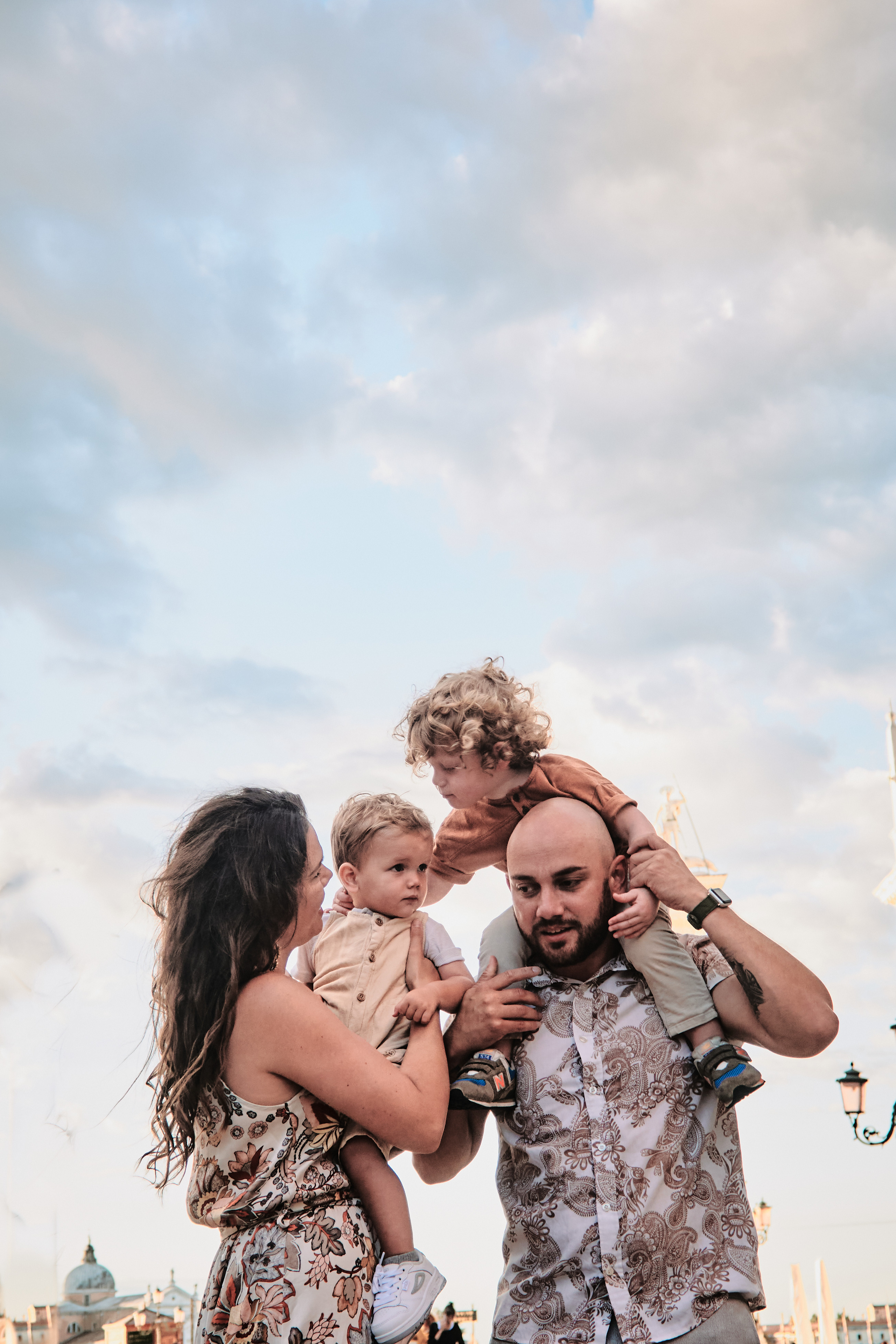 This family photo captures a beautiful moment on San Marco Square in Venice. The parents stand with their two children, all of them looking joyful and content. In the background, the grandeur of Venice's architecture can be seen, adding to the beauty of the scene.