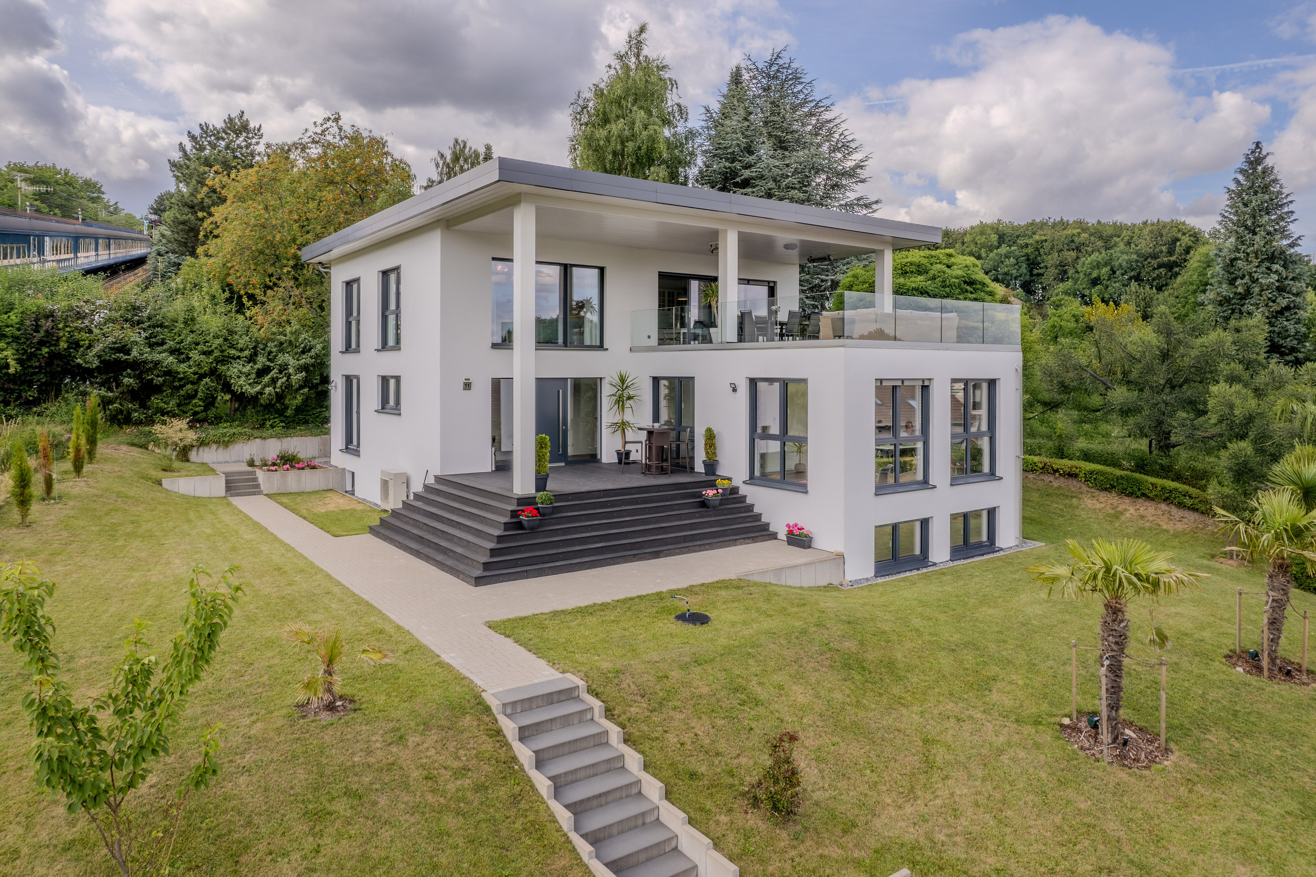 Modernes zweistöckiges Einfamilienhaus mit großen Panoramafenstern, überdachter Terrasse und gepflegtem Garten in ruhiger, grüner Umgebung.