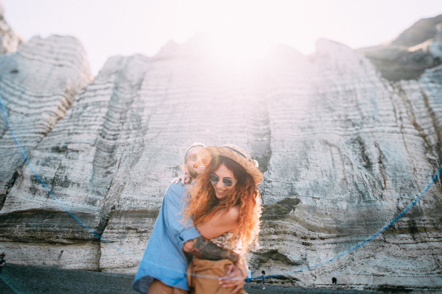 The groom kisses the bride on the neck, the bride smiling and her red hair blowing in the wind.