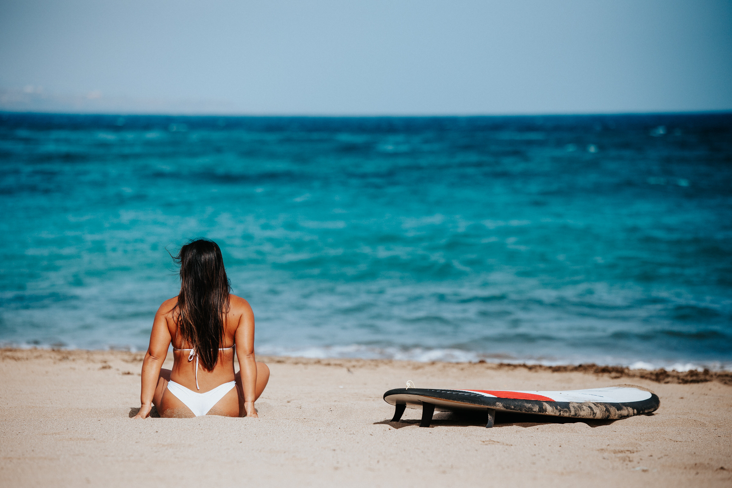 A photo tour of the beach in Gran Canaria A woman in a bikini sits on the beach next to a surfboard.