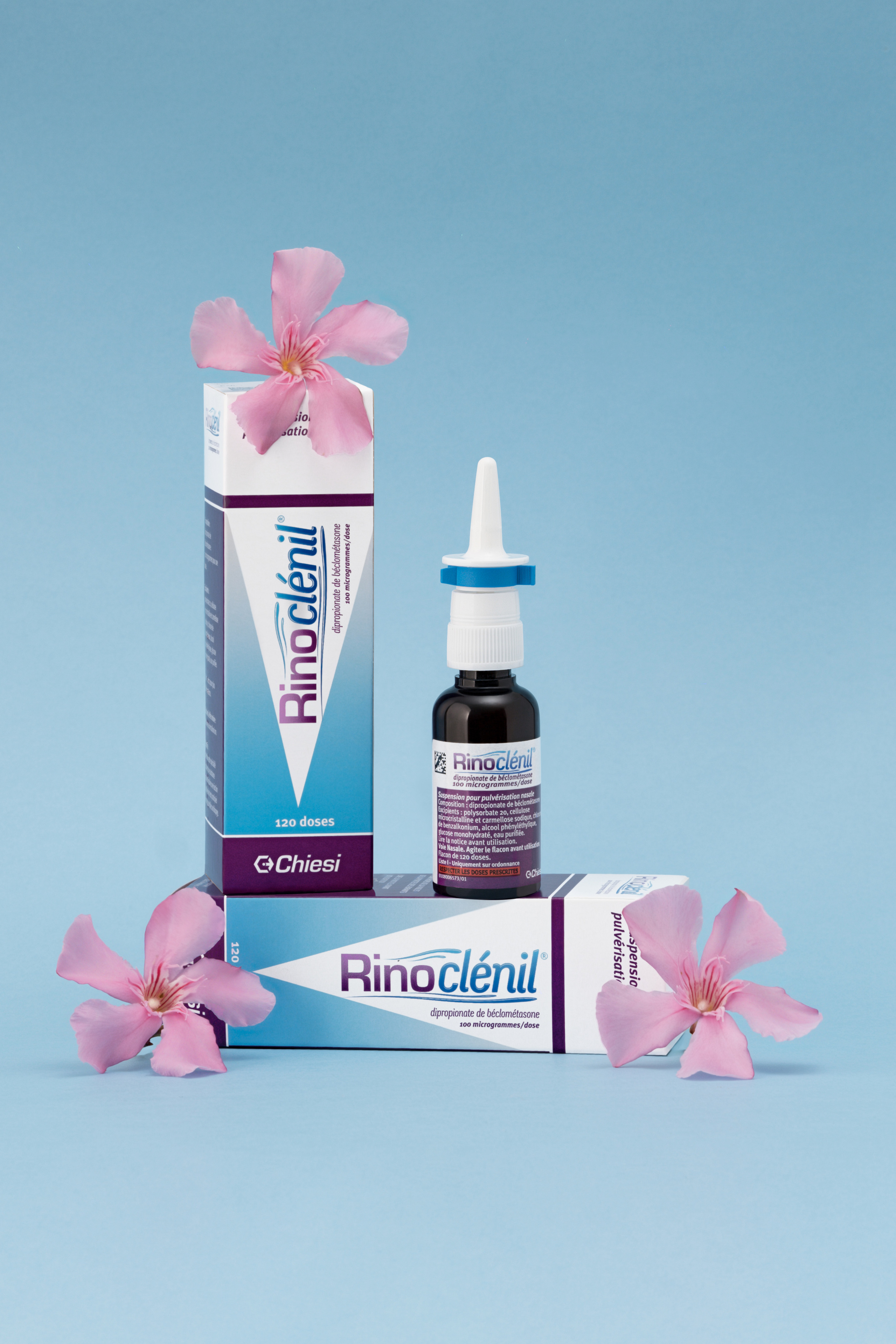 Photographie de produit Rhinoclénil sur le fond uni bleu ciel entouré de fleurs roses par photographe de produit en France