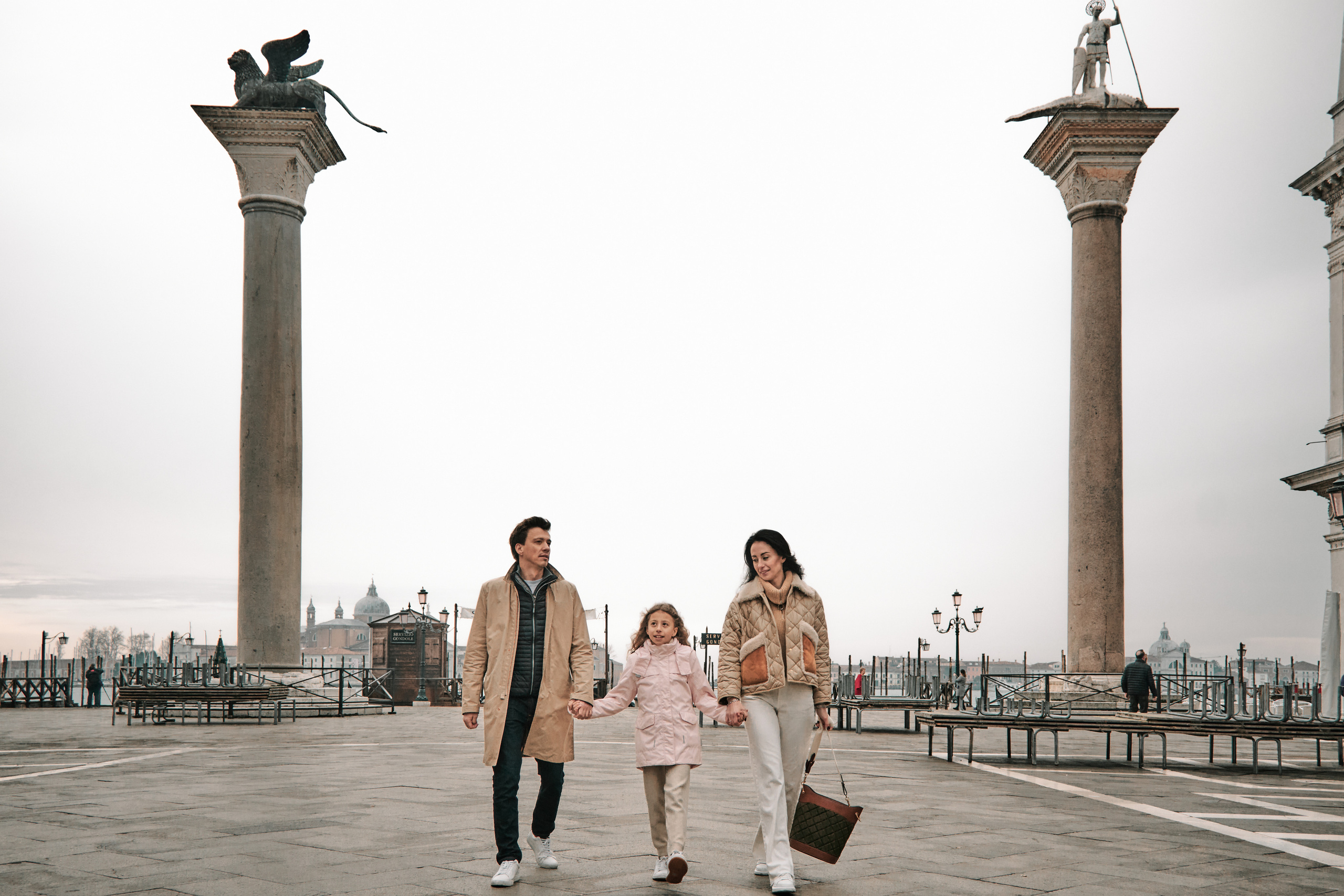 A happy family of four stands on San Marco Square, the children smiling and looking directly into the camera as their parents hold them close. In the background, the iconic architecture of Venice can be seen. Italy, photographer of Venice, family photoshoot