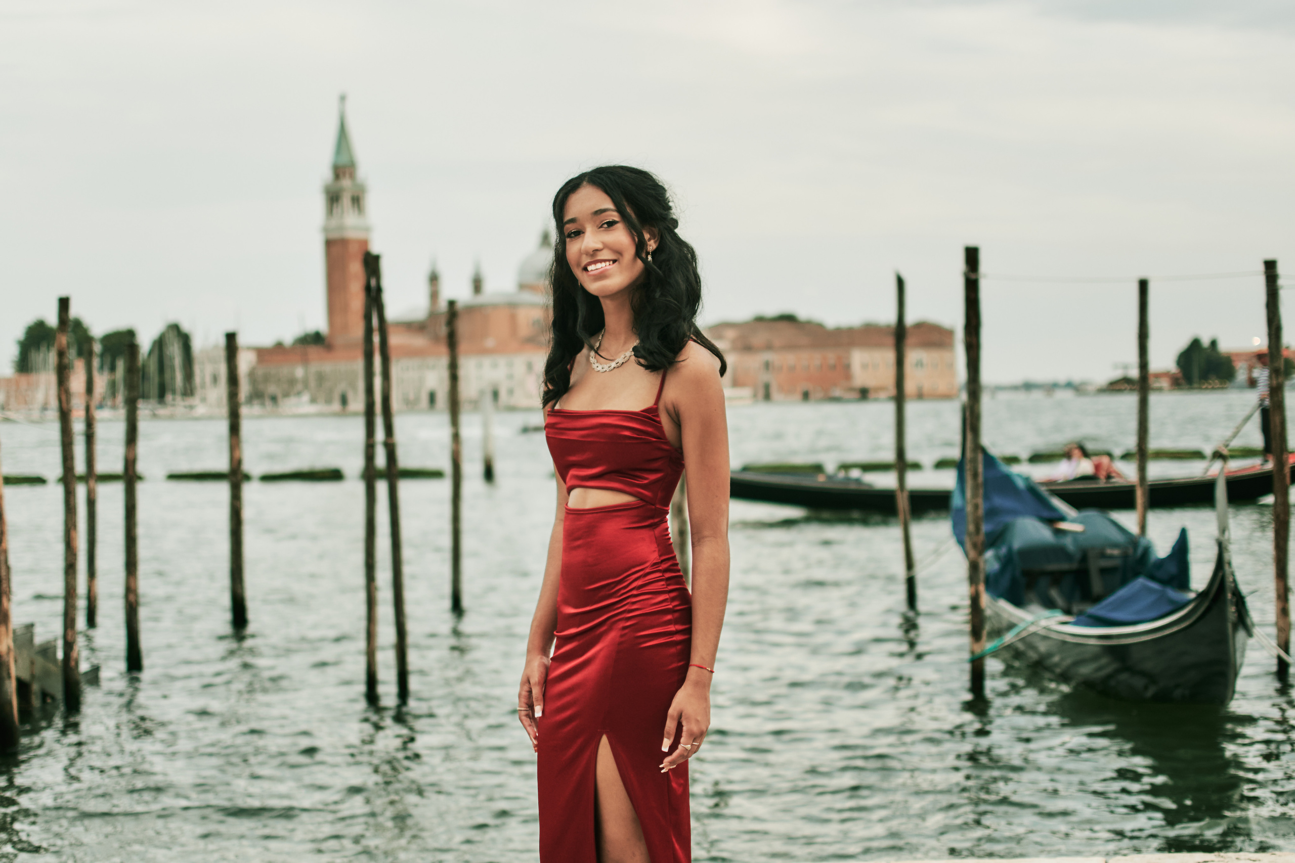 Enchanting girl in a vibrant red dress strolls along Venice's picturesque narrow canals.
