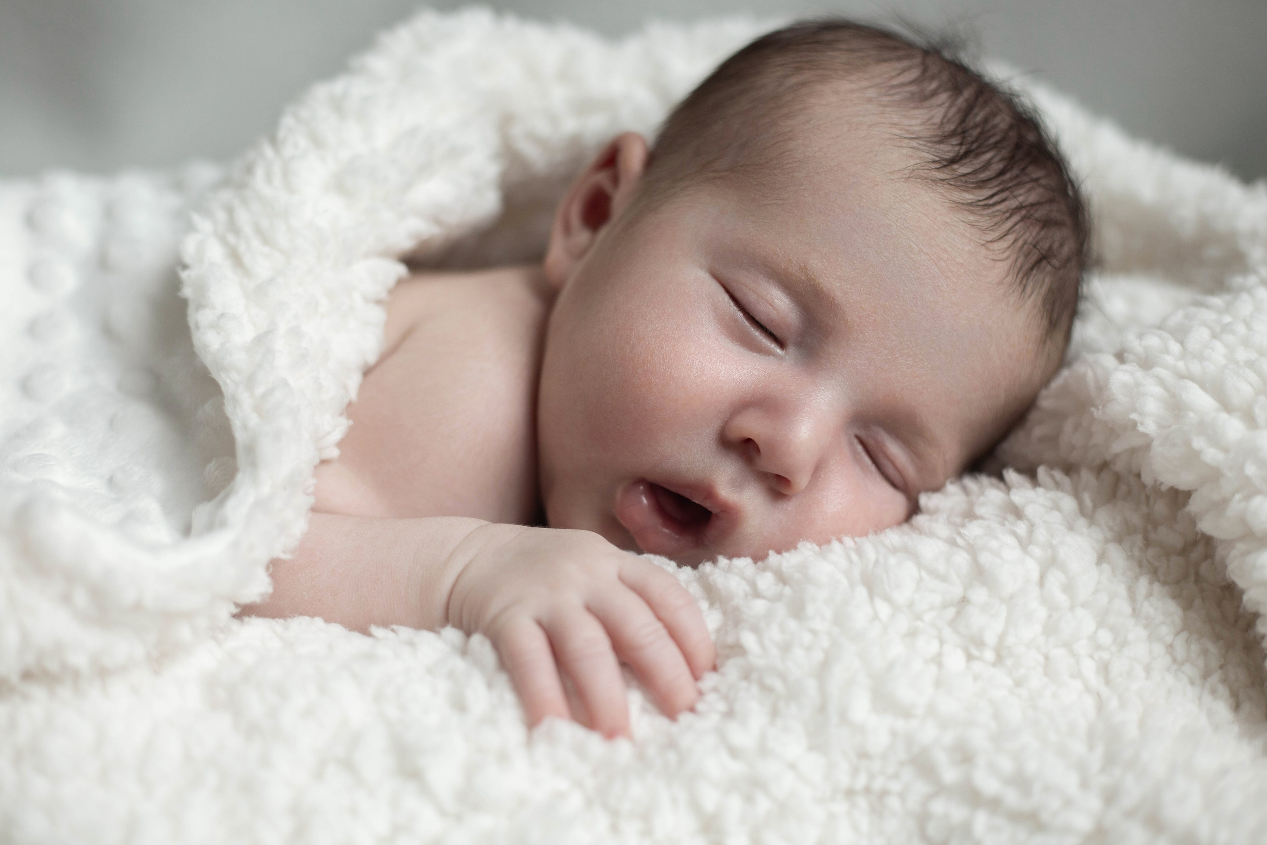 Photo de bébé qui dort sous un plaid doux, moment tendre de la séance nouveau-né