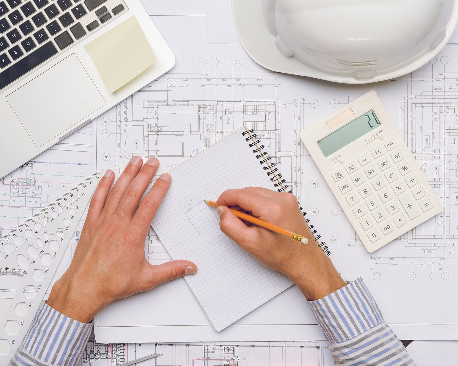 Hands sketching renovation plans on blueprints with a calculator, symbolizing detailed cost estimation for Athens property projects.