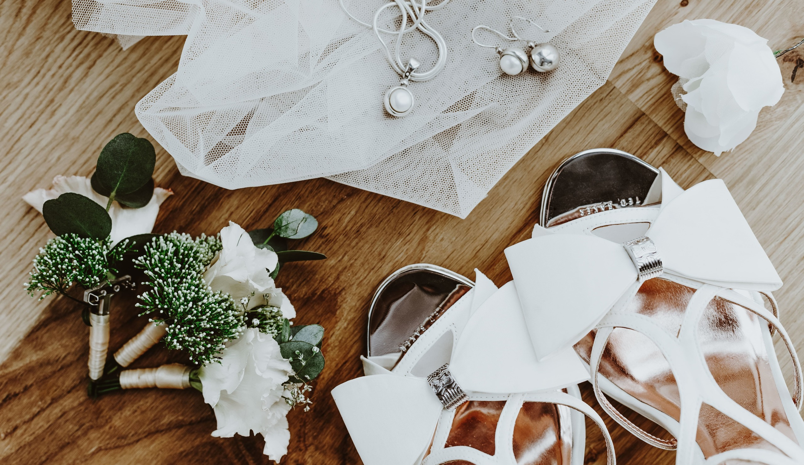 Elegante Brautschuhe stehen neben einer zarten Boutonniere – stilvolle Hochzeitsdetails.