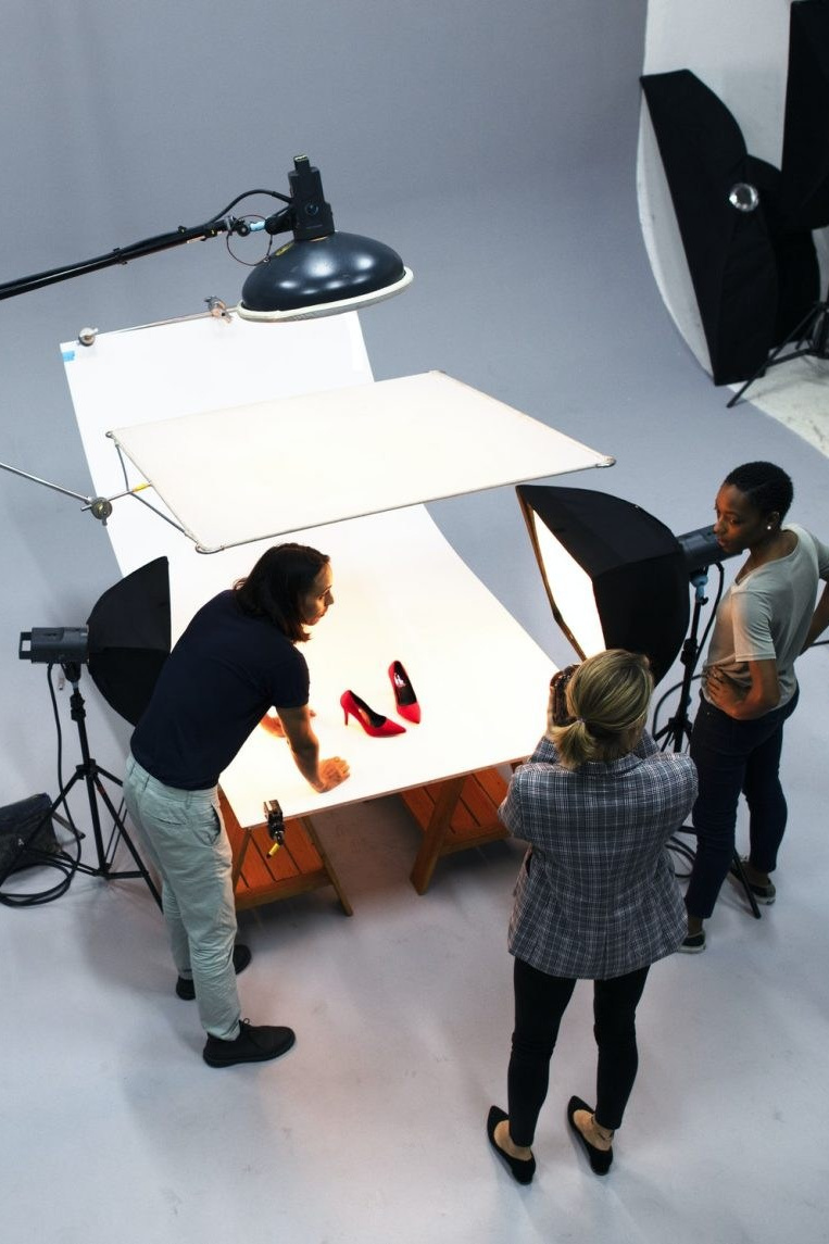 Studio team working on a product photoshoot featuring red shoes, surrounded by professional lighting and equipment