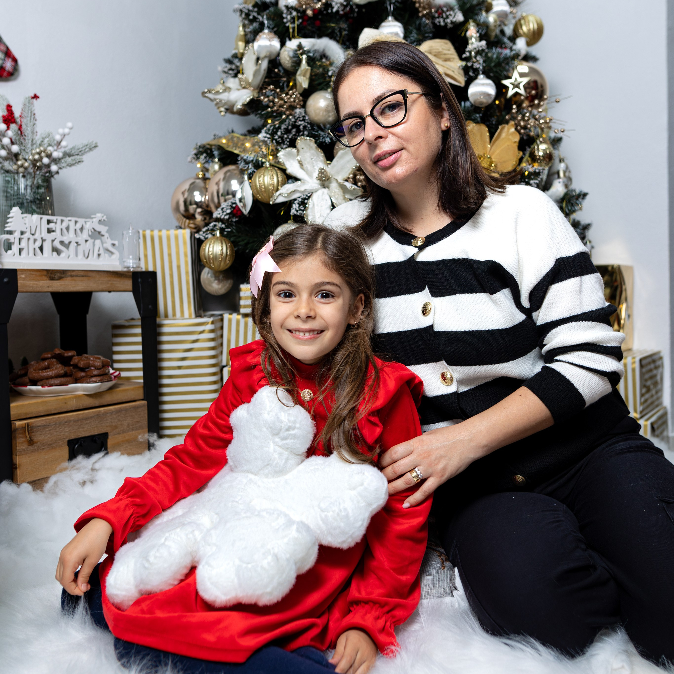 Ședință foto de Crăciun în studio, familie zâmbitoare lângă brad împodobit, decor festiv și lumini calde de sărbătoare