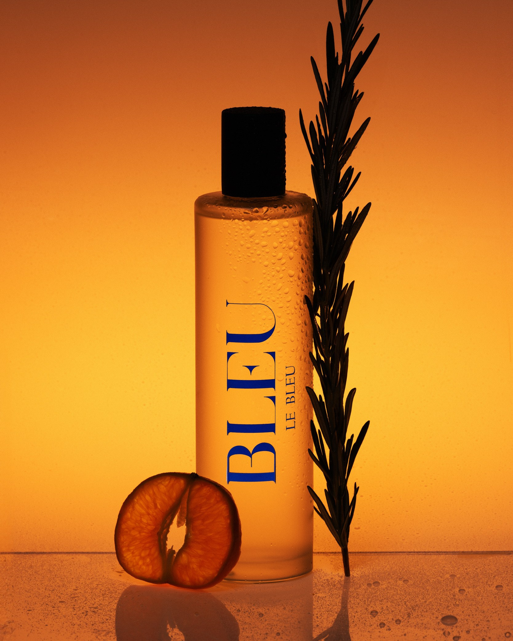 Perfume bottle labeled Bleu with rosemary and orange slice on a warm gradient background
