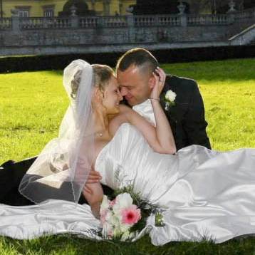 Red-haired bride holding her flowing veil aloft smiles seductively to her bouquet holding groom as he leans back against a railing in appreciation at the Vrtba Garden in Prague. 