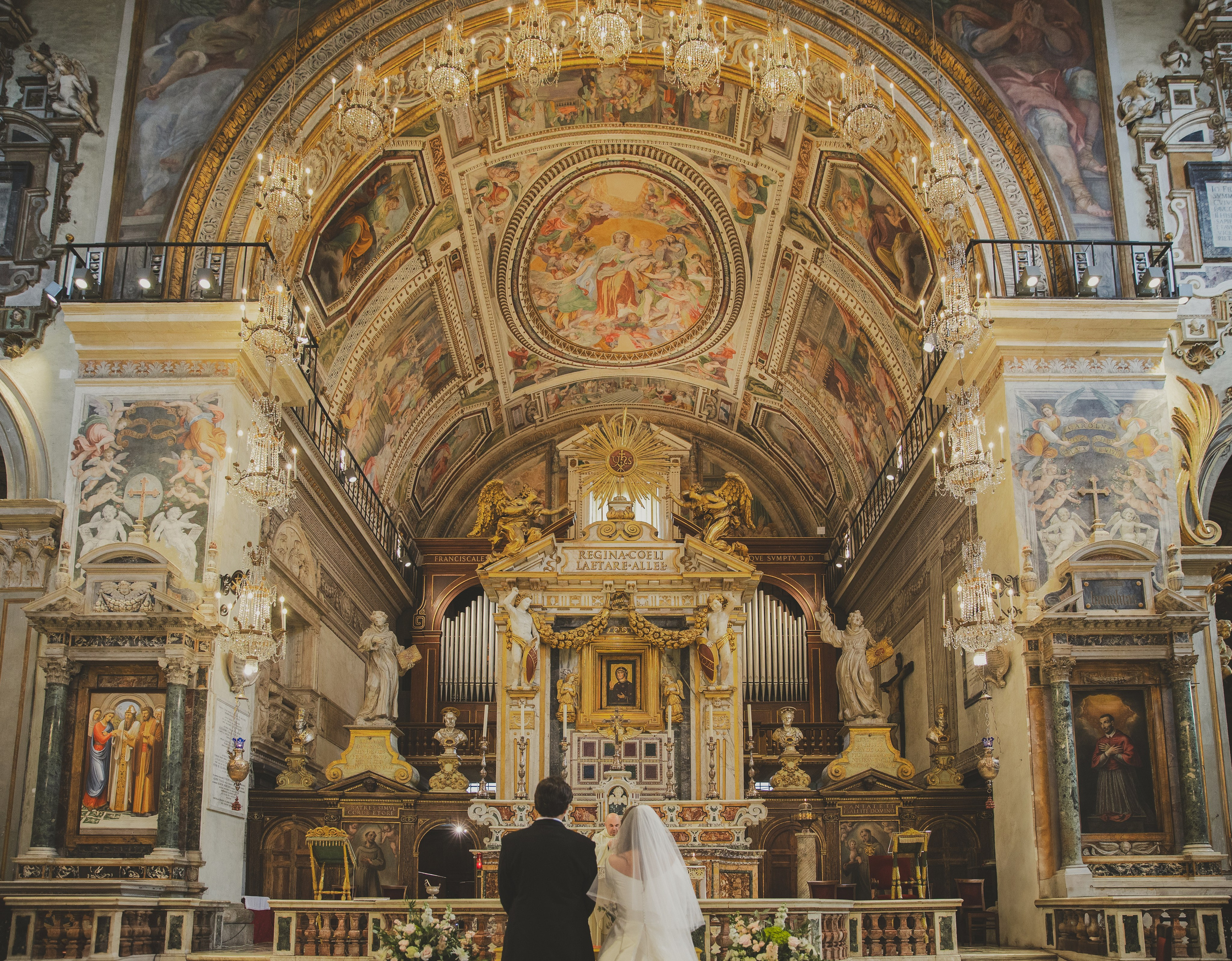 Couple exchanging vows at the altar in Santa Maria in Aracoeli, surrounded by chandeliers in a romantic atmosphere.