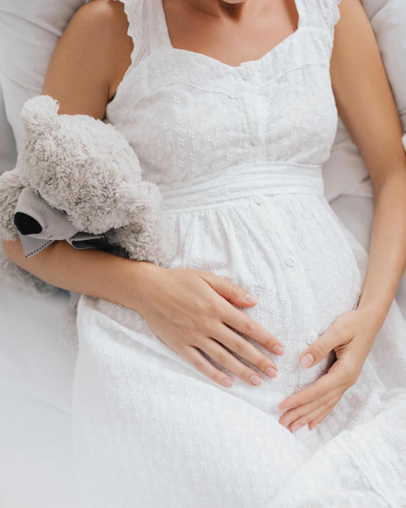 Maternity portrait featuring white dress and childhood teddy
