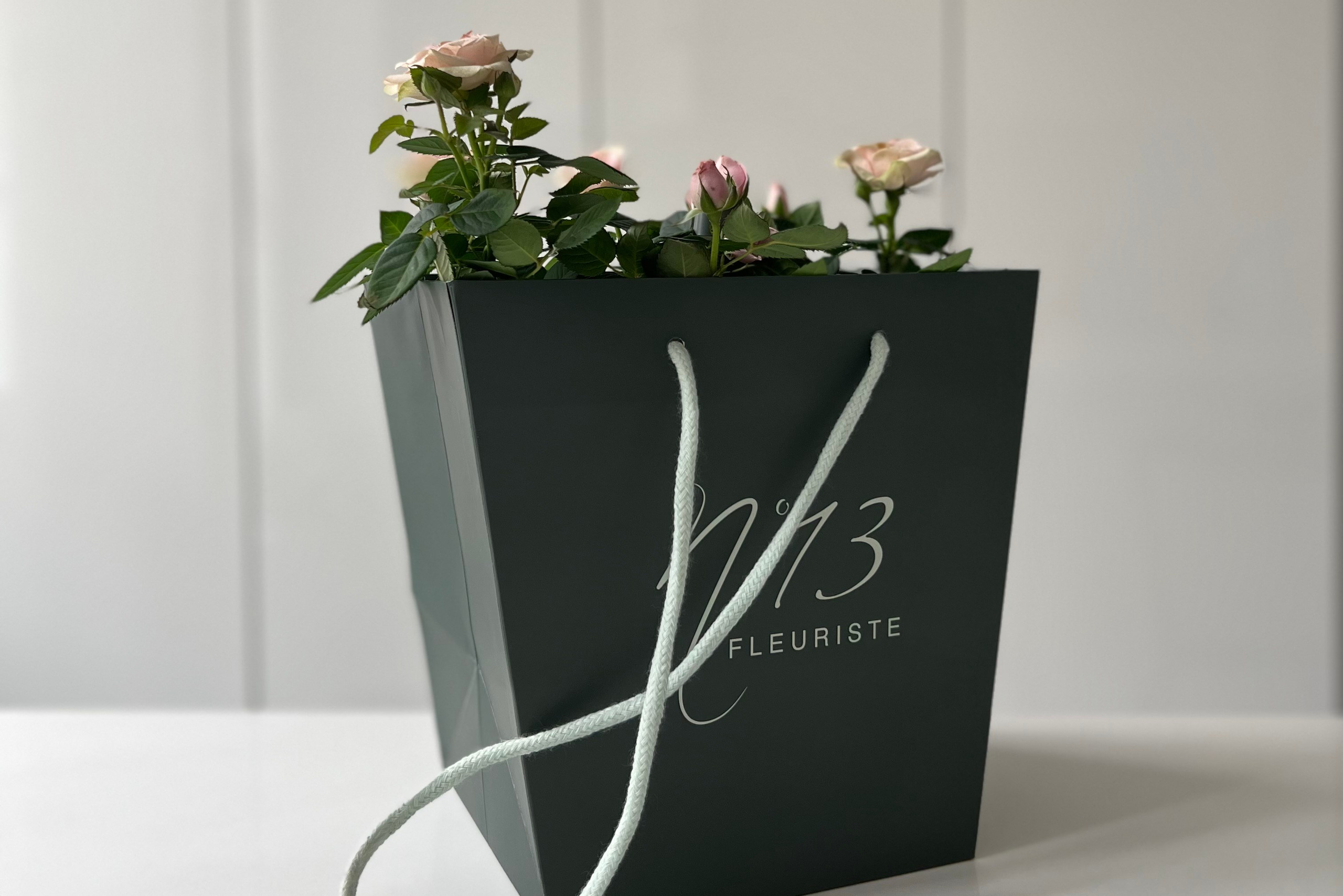 Photographie d’un sac cadeau noir avec des fleurs fraîches – mise en scène minimaliste et élégante sur fond blanc