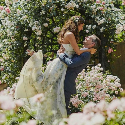 Red-haired bride holding her flowing veil aloft smiles seductively to her bouquet holding groom as he leans back against a railing in appreciation at the Vrtba Garden in Prague. 