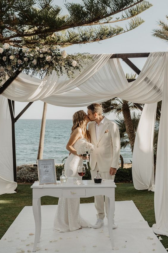 Wedding ceremony on the beach groom and bride kiss under the wedding arch