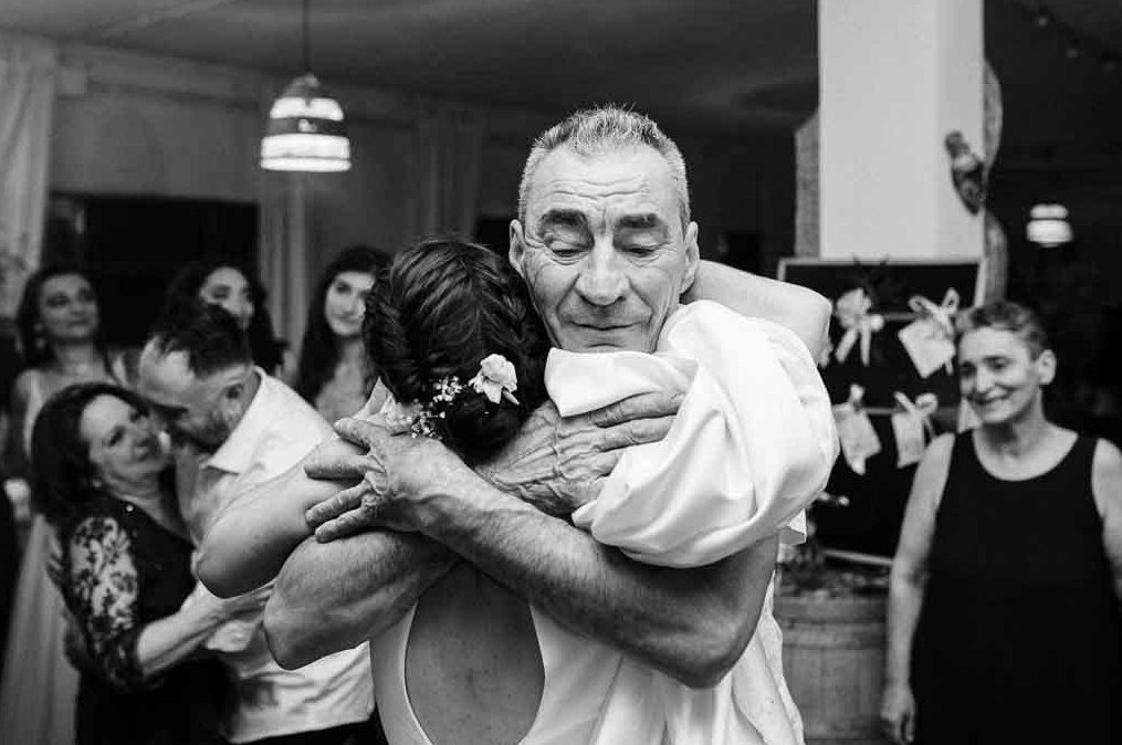 Un toccante abbraccio tra la sposa e suo padre durante la festa di matrimonio, catturato in un sentito scatto in bianco e nero che riflette l'emozione e il calore di questo speciale legame familiare
