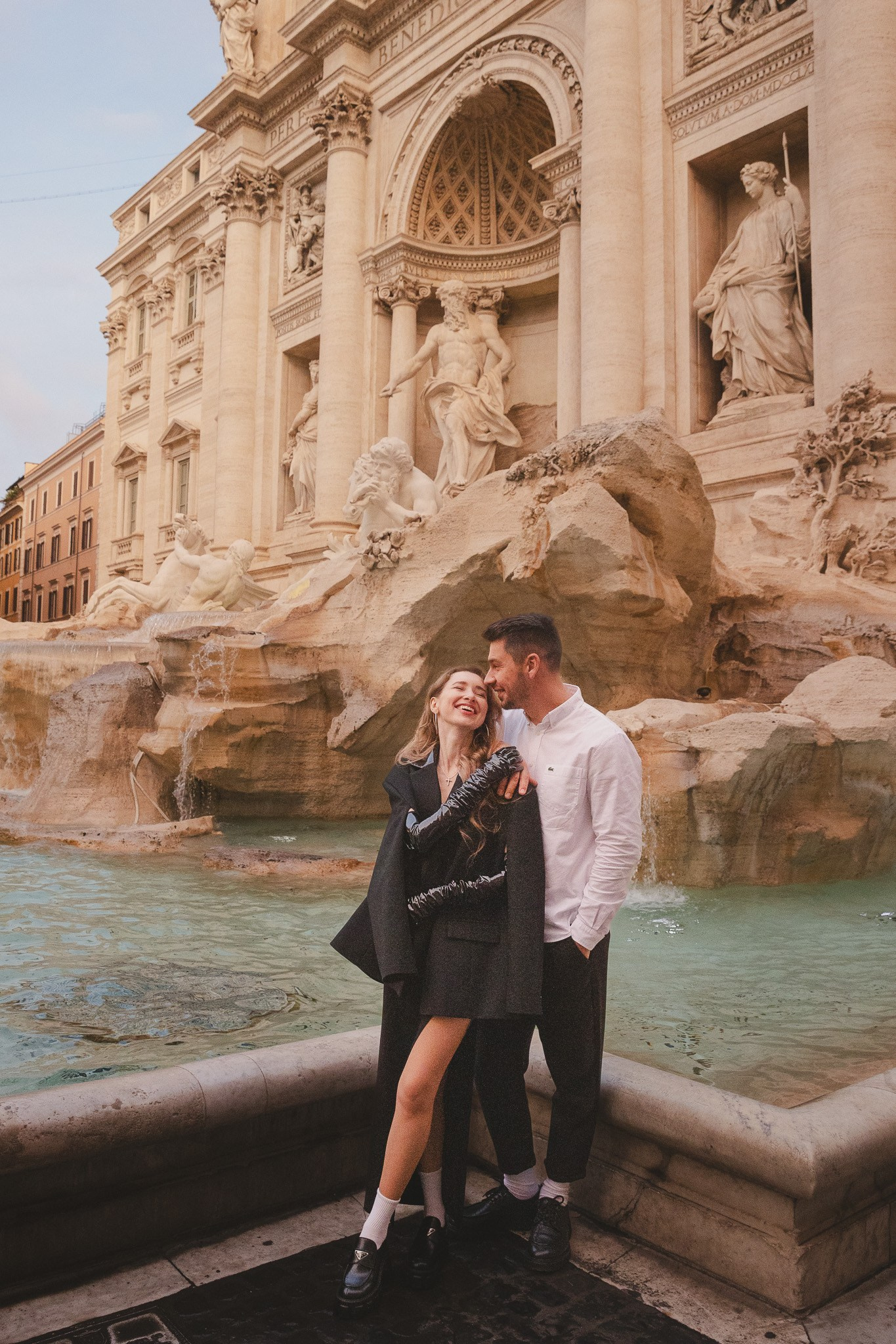 A couple embracing in front of the Trevi Fountain at sunrise lost in the moment.
