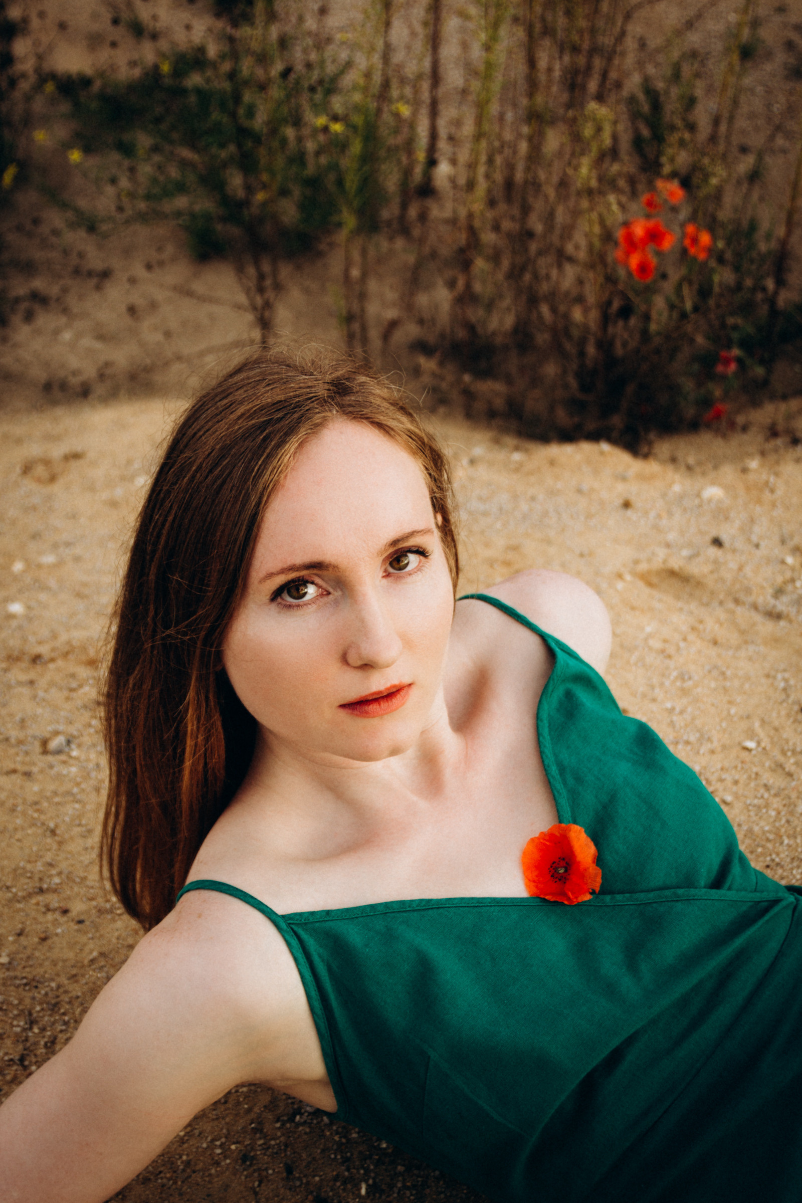 Ausdrucksstarkes Portrait einer jungen Frau in grünem Kleid mit Mohnblume – entstanden bei einem natürlichen Frauenfotoshooting im Freien.