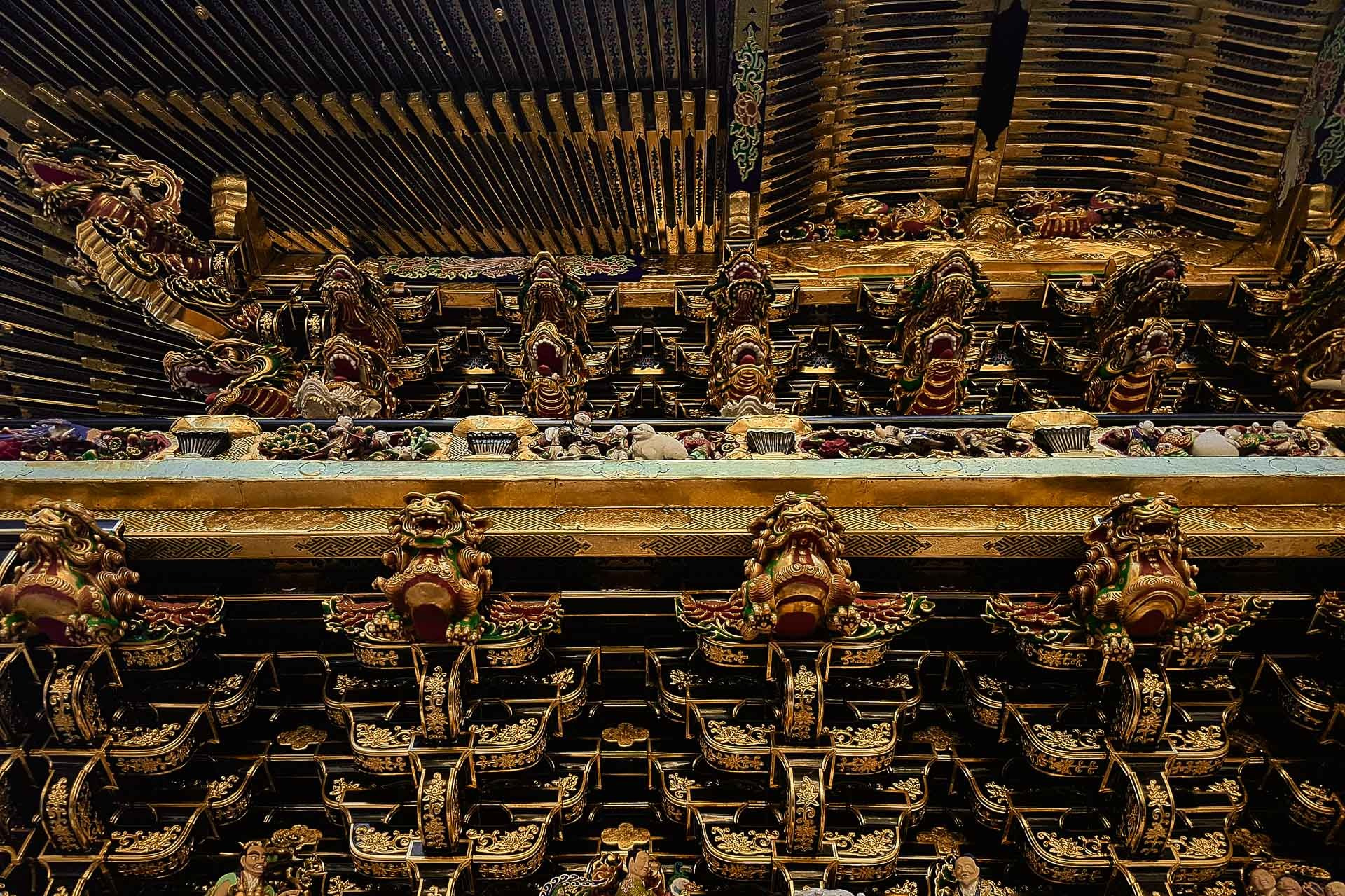 Golden Yomeimon Gate at Toshogu Shrine in Nikko surrounded by tall cedar trees.